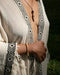 Person wearing a patterned garment with fringe details, holding hands together.
