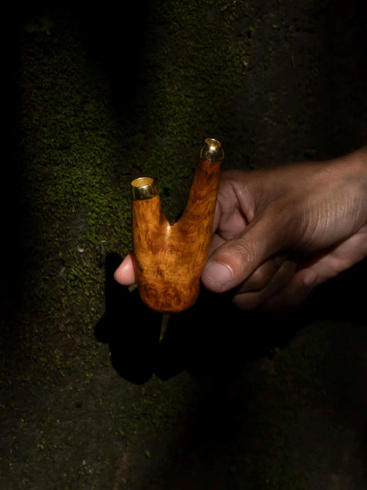 Hand holding a wooden pipe against a dark background