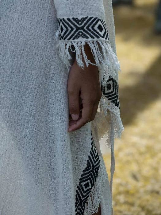 Close-up of a white garment with black geometric patterns and fringes, held by a person.