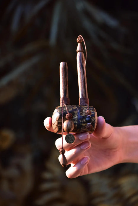 Hand holding a wooden tool with decorative elements against a dark background