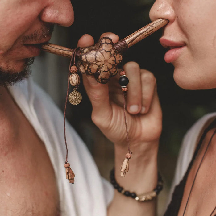 Two people sharing a wooden pipe with decorative elements.
