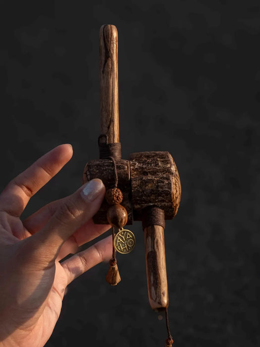 Hand holding a wooden prayer wheel against a dark background