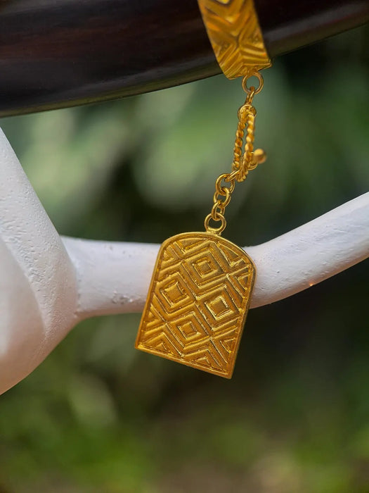 Gold pendant hanging from a branch with a blurred natural background