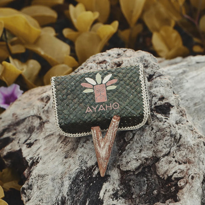 Green woven handbag with 'AYAHO' branding on a textured rock surface with blurred yellow flowers in the background.