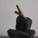 Two sticks balanced on top of a black stone against a gray background