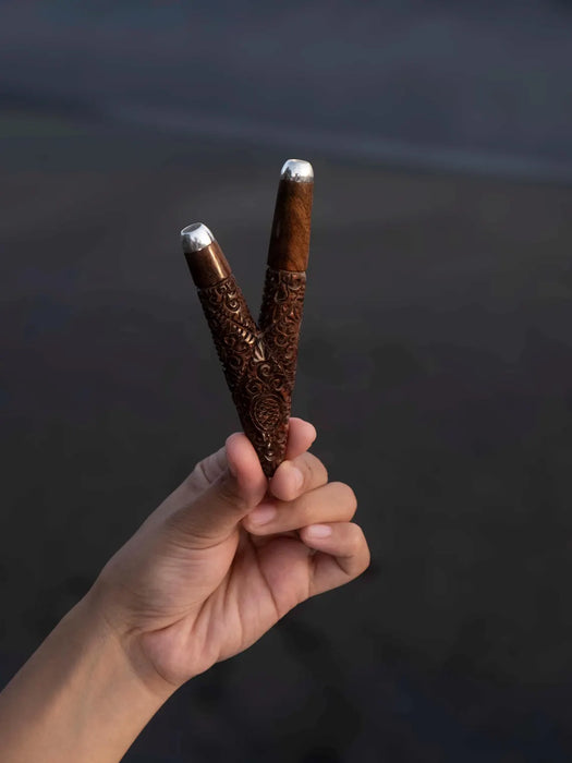 Hand holding two intricately carved wooden sticks with silver tips against a dark background