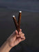 Hand holding two intricately carved wooden sticks with silver tips against a dark background