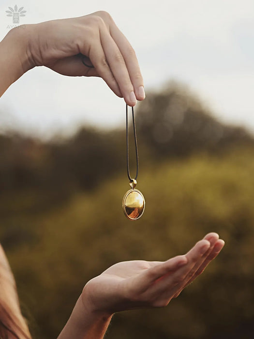 Hand holding a gold necklace with a pendant against a blurred natural background