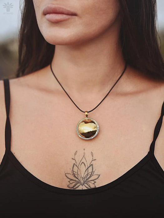 Woman wearing a black tank top with a gold pendant necklace, showing a tattoo on her chest.