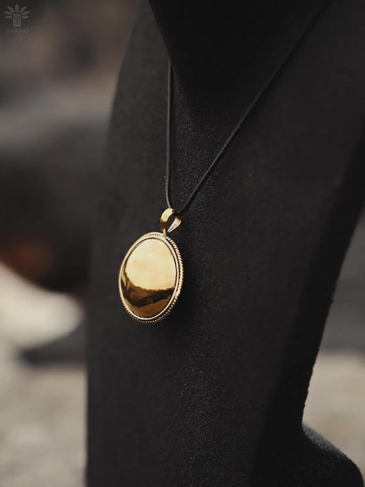 Gold pendant on a black cord against a blurred background