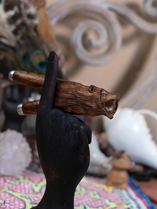 Handmade wooden object held by a black-gloved hand against a decorative background