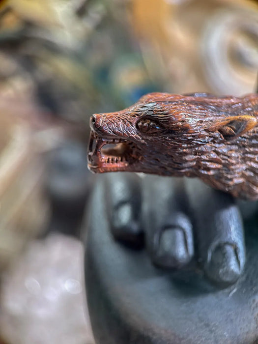 Close-up of a hand holding a wooden wolf figurine with a blurred background