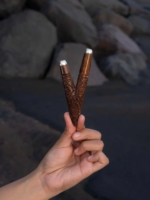 Hand holding two intricately designed wooden sticks with a blurred natural background
