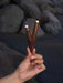 Hand holding two intricately designed wooden sticks with a blurred natural background