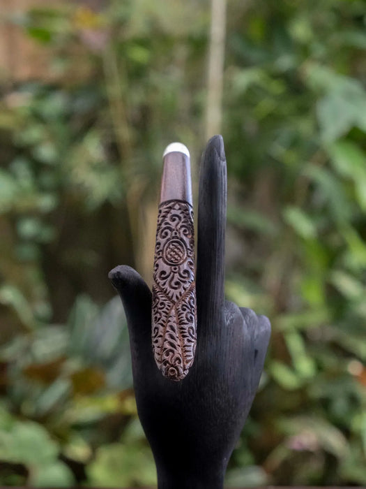 Decorative ring on a black-gloved hand against a blurred natural background