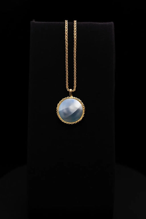 Gold necklace with a blue pendant on a black background
