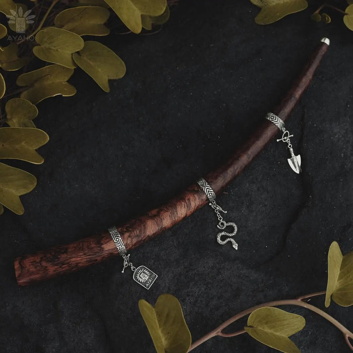Silver bracelet with charms on a wooden stick against a dark background with green leaves.
