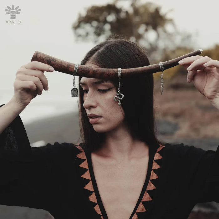 Woman holding a wooden staff with earrings against a blurred natural background