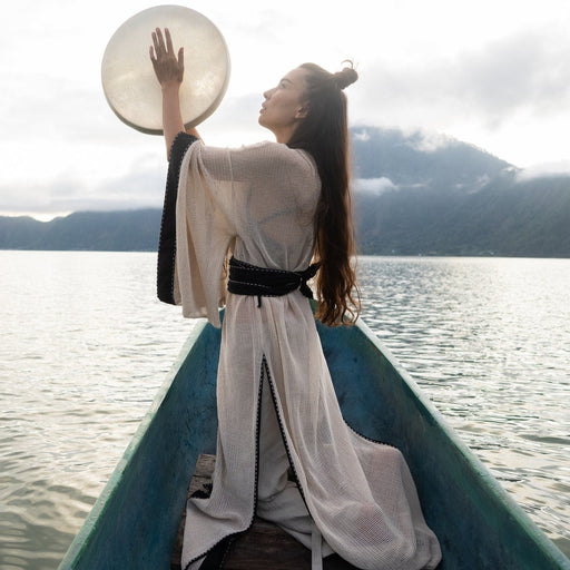 A figure stands poised on a boat, draped in a long cotton shibori kimono cardigan, embodying the chic spirit of Boheme as a ritual robe and beach coverup