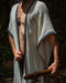 A man stands in a forest, his demeanor calm and grounded, wearing a Boho tribal cotton poncho, embodying a unisex, earthy shamanic style.