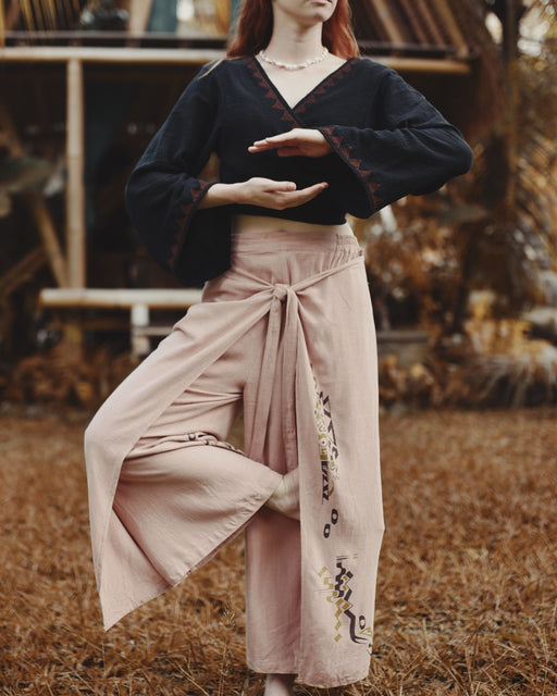 Person wearing a dark sweater and light pink pants with floral embroidery in an outdoor setting.