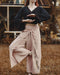 Person wearing a dark sweater and light pink pants with floral embroidery in an outdoor setting.