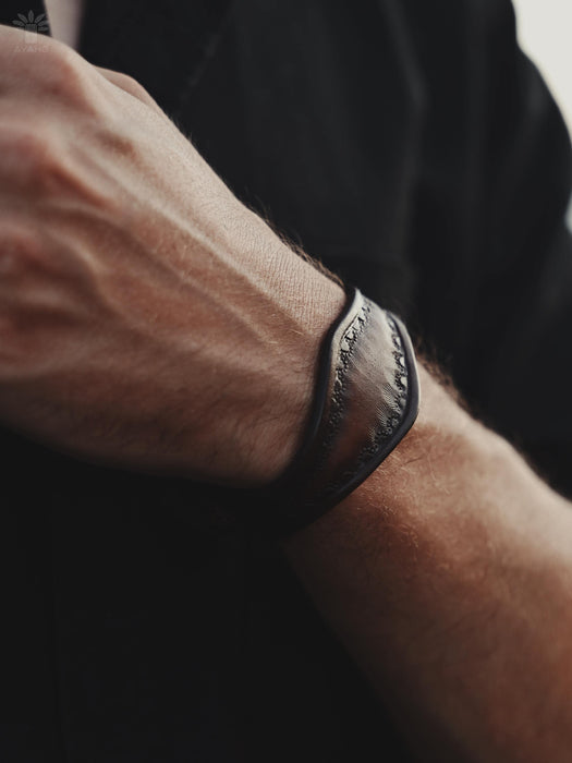 A spiritual tool in the form of a dark buffalo leather bracelet with a triple-infinity symbol, handcrafted for modern men.