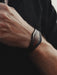 A spiritual tool in the form of a dark buffalo leather bracelet with a triple-infinity symbol, handcrafted for modern men.