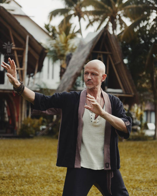 Man practicing martial arts in a tropical setting with palm trees and wooden structures.
