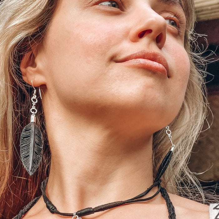 Woman wearing a black feather necklace and matching earrings, presenting a boho style with elements of shamanic jewelry, creating an aesthetic rooted in natural motifs