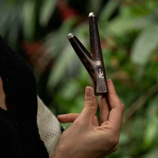 Elite rosewood kuripe pipe with intricate Shipibo patterns, held aloft, a sophisticated tool for hape snuff and a testament to shamanic craftsmanship.