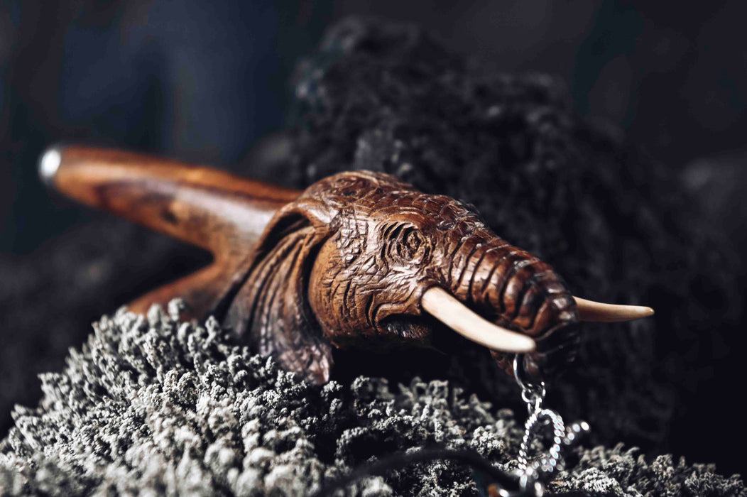 a wooden kuripe elephant pipe, designed for hape snuff application. The kuripe, linked to a charm-adorned necklace, serves as a unique, handmade smoking accessory and part of a shamanic protection kit, blending herbal medicine traditions