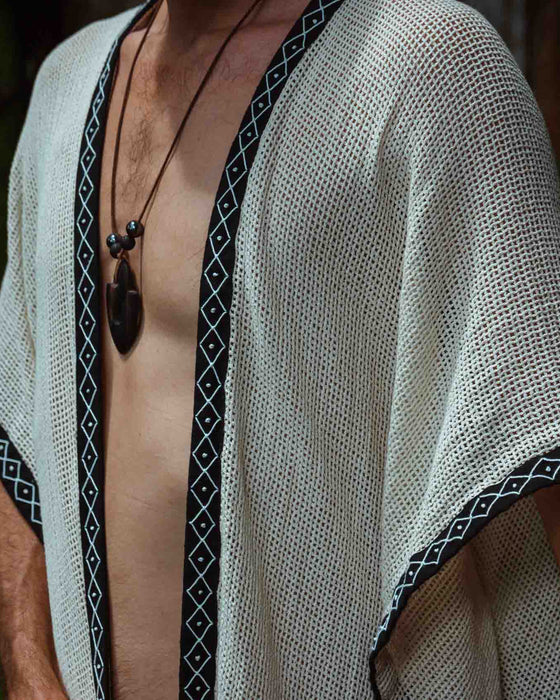A person enveloped in a handmade Boho tribal cotton poncho, embracing the serenity of nature at a waterfall, reflecting a unisex shamanic clothing style