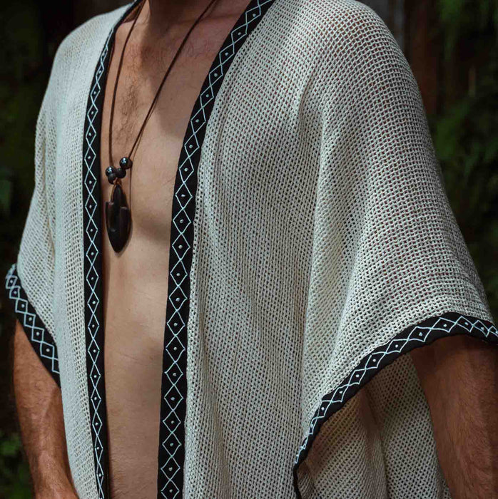 A person enveloped in a handmade Boho tribal cotton poncho, embracing the serenity of nature at a waterfall, reflecting a unisex shamanic clothing style