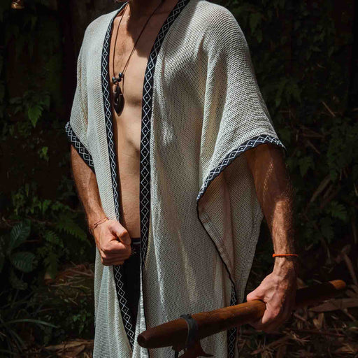 A person enveloped in a handmade Boho tribal cotton poncho, embracing the serenity of nature at a waterfall, reflecting a unisex shamanic clothing style