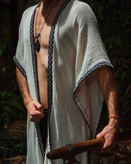 A person enveloped in a handmade Boho tribal cotton poncho, embracing the serenity of nature at a waterfall, reflecting a unisex shamanic clothing style