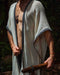 A person enveloped in a handmade Boho tribal cotton poncho, embracing the serenity of nature at a waterfall, reflecting a unisex shamanic clothing style