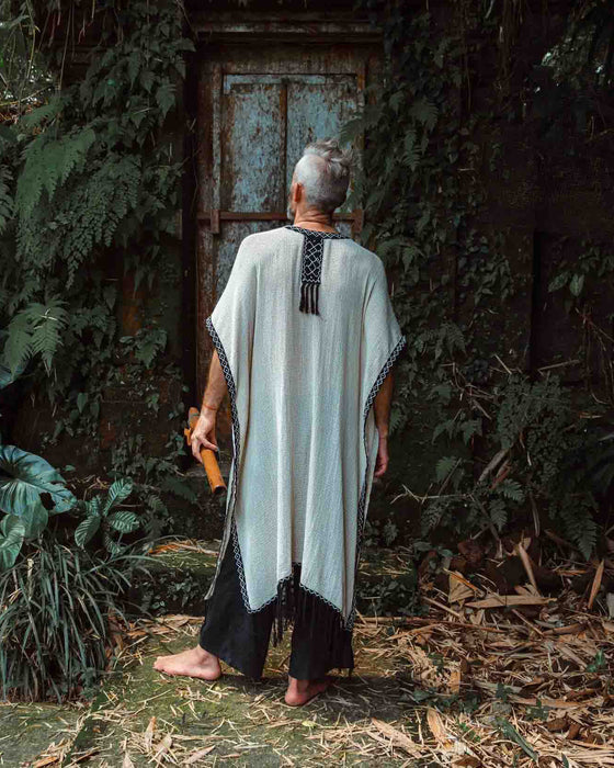 A person enveloped in a handmade Boho tribal cotton poncho, embracing the serenity of nature at a waterfall, reflecting a unisex shamanic clothing style