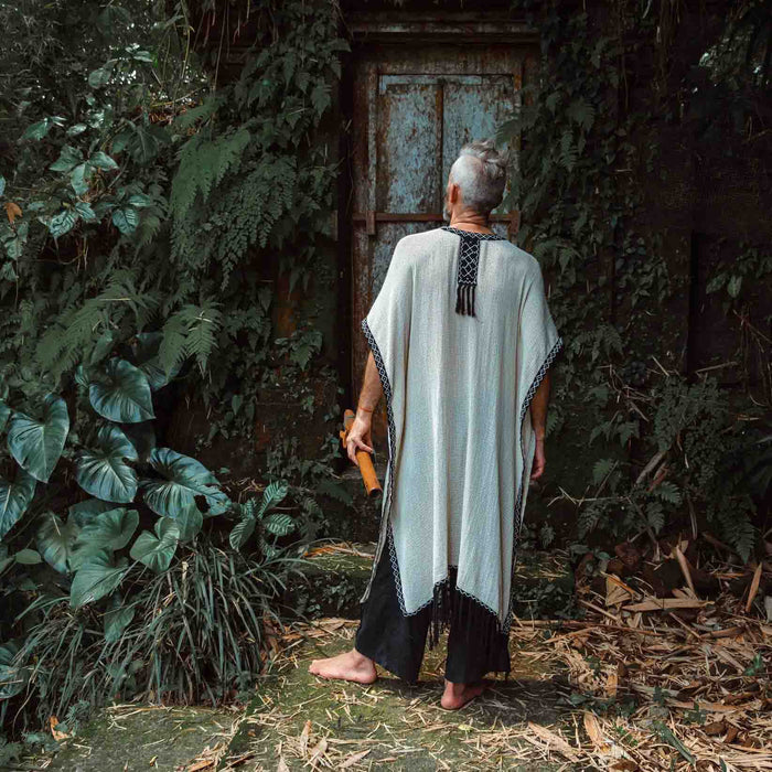 A person enveloped in a handmade Boho tribal cotton poncho, embracing the serenity of nature at a waterfall, reflecting a unisex shamanic clothing style