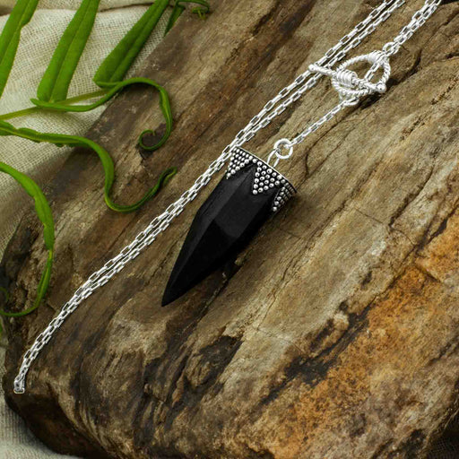 Sterling silver capped black onyx pendulum necklace, resting on petrified wood, a magic item used for divination and enhancing psychic abilities
